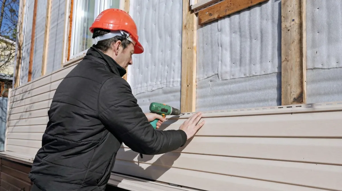 Siding replacement professional using a power drill to install new tan vinyl siding on a home exterior in Jackson, MS